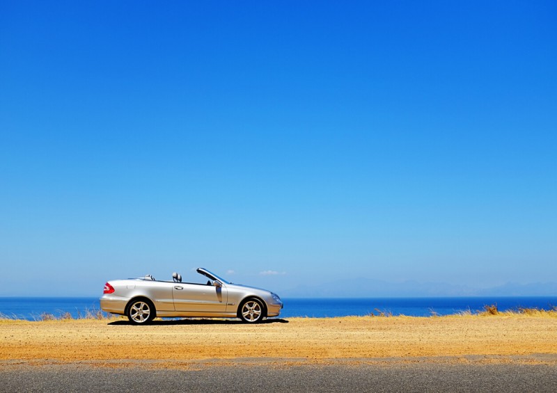 Convertible car parked near the coast with blue sky