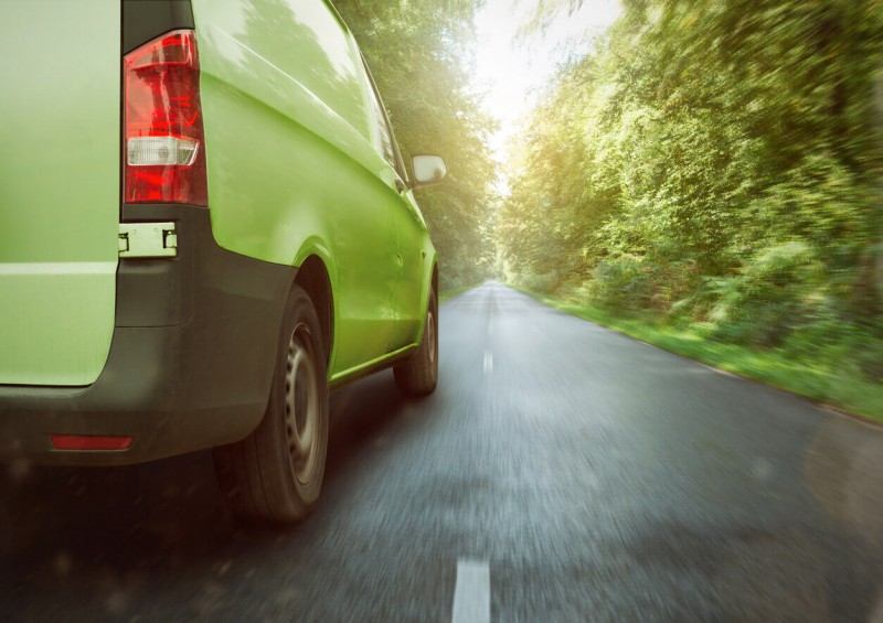 Green van driving with forest on both sides