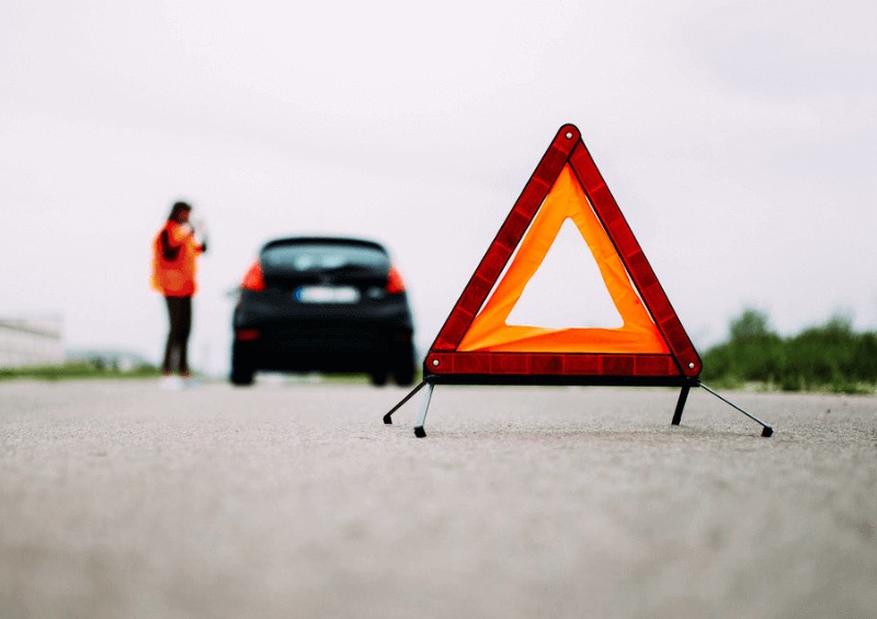 Person waiting by their broken down car and safety triangle